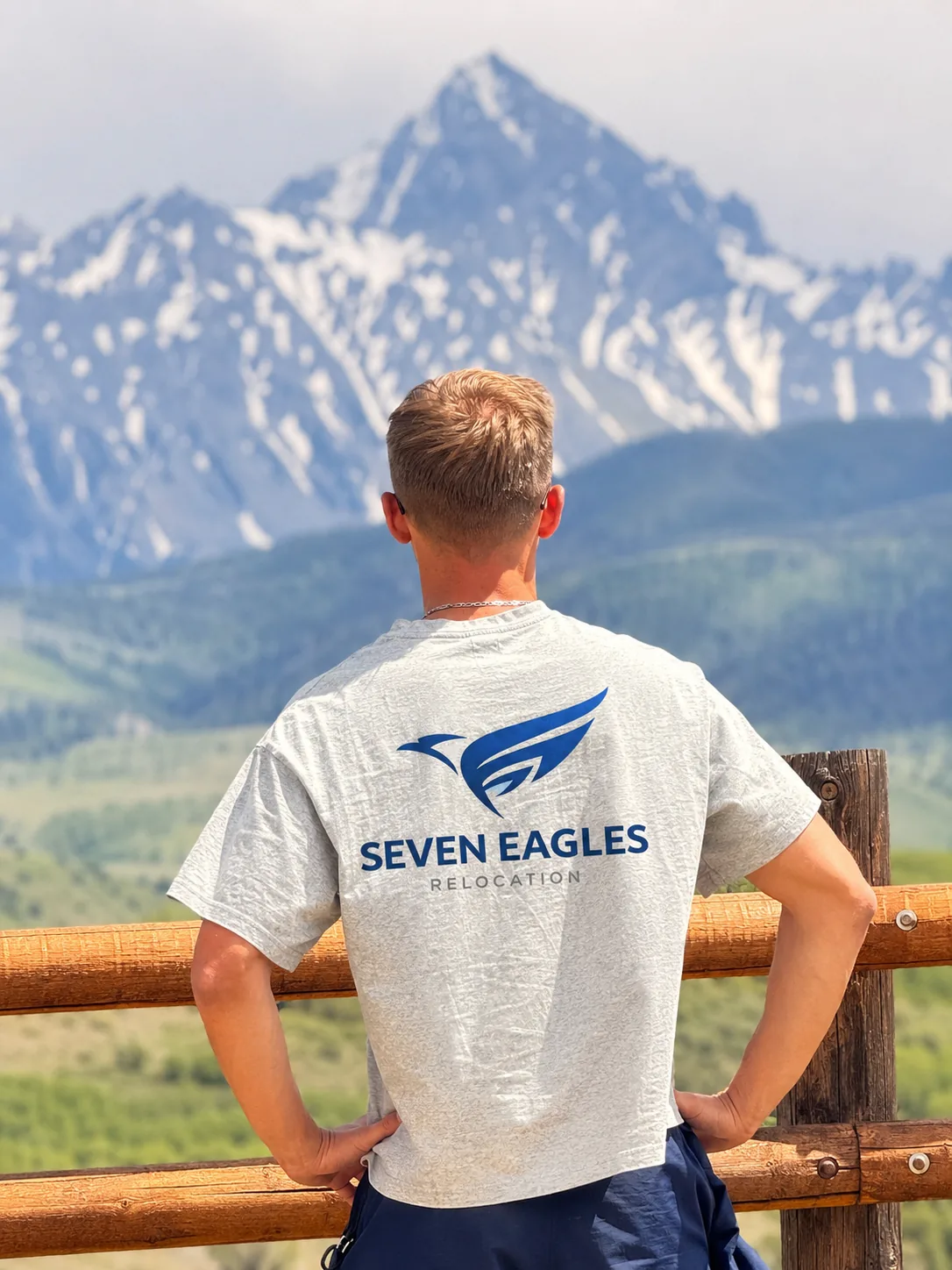 Seven Eagles Relocation founder at a Colorado mountain overlook, the company eagle logo on the back of his shirt